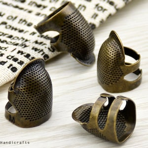 May include: Four antique gold-toned thimbles for sewing. The thimbles have a textured surface and are designed to fit on the finger.
