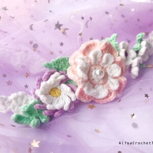 May include: A crocheted flower crown with pink, white, and green flowers. The crown is on a purple background with silver glitter stars.