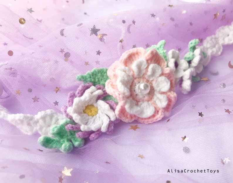 May include: A crocheted flower crown with pink, white, and green flowers. The crown is on a purple background with silver glitter stars.