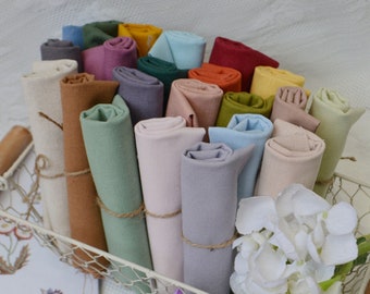 Puede incluir: Una cesta llena de rollos de tela en varios colores, incluyendo beige, marrón, verde, azul y gris. La tela está dispuesta en un patrón circular, con los extremos de los rollos atados con cuerda.