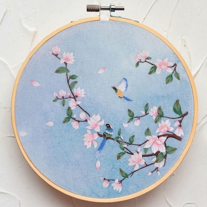 Peut inclure: Un cerceau de broderie bleu et blanc avec un motif floral et deux oiseaux. Les fleurs sont roses et blanches et les oiseaux sont bleus, verts et jaunes.