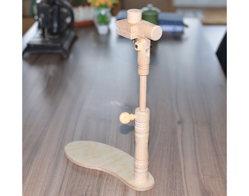 May include: A wooden embroidery stand with a base and a vertical post that adjusts in height. The stand has a knob for tightening the post and a clamp at the top for holding embroidery hoops.