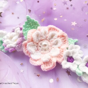 May include: A crocheted flower crown with pink, white, and green flowers. The crown is on a purple tulle background with silver glitter stars.