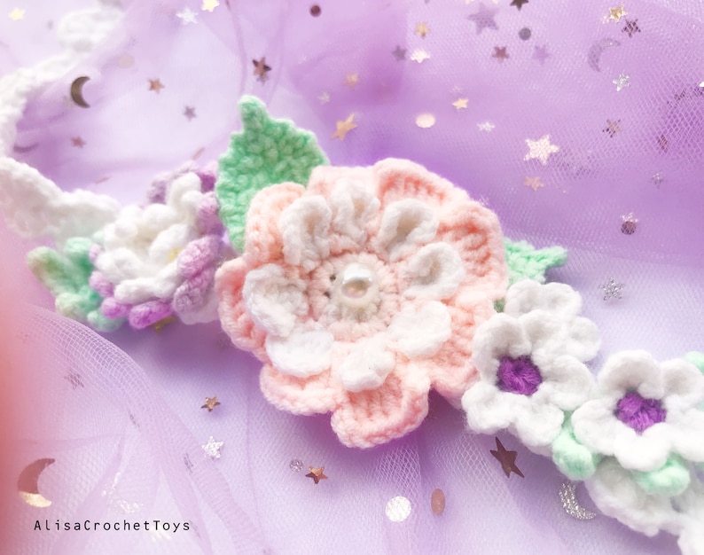 May include: A crocheted flower crown with pink, white, and green flowers. The crown is on a purple tulle background with silver glitter stars.