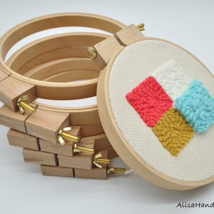 May include: A set of four wooden embroidery hoops with a finished embroidery project in one of the hoops. The embroidery is a geometric design of four squares in red, white, blue, and yellow yarn.
