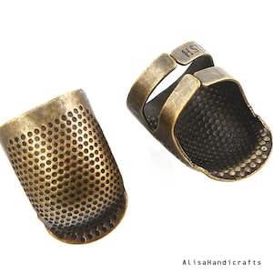 May include: Two antique gold thimbles, one with a closed top and the other with an open top and a finger loop. Both thimbles have a textured surface.