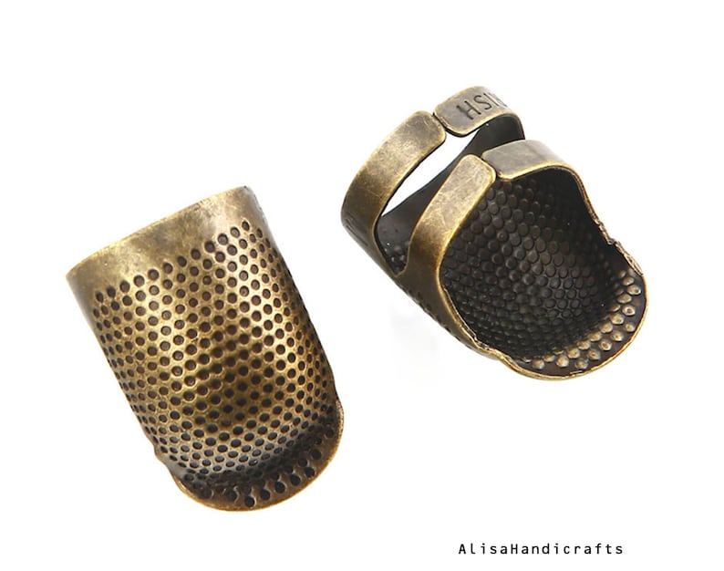 May include: Two antique gold thimbles, one with a closed top and the other with an open top and a finger loop. Both thimbles have a textured surface.
