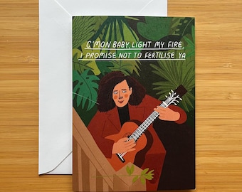 May include: Greeting card with a whimsical illustration of a person playing a guitar. The card features the text "C'mon baby, light my fire, I promise not to fertilise ya" against a backdrop of lush green foliage. Includes a white envelope.