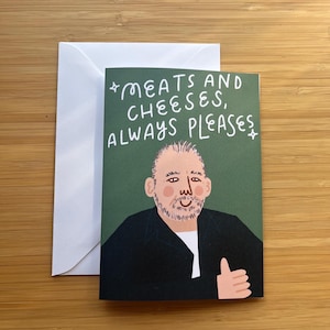 May include: A greeting card with a green background and the text "MEATS AND CHEESES, ALWAYS PLEASES." The card features an illustration of a man giving a thumbs up. A white envelope is behind the card.
