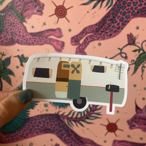 May include: A white vintage camper van sticker with brown and green doors, a red awning, and a flower design. The sticker has a white border and is on a pink and green background.