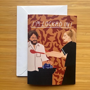 May include: Greeting card with the text "I'M LOCKED IN!" featuring an illustration of two people. One person is holding a spoon, and the other is receiving the spoon. The card is accompanied by a white envelope.