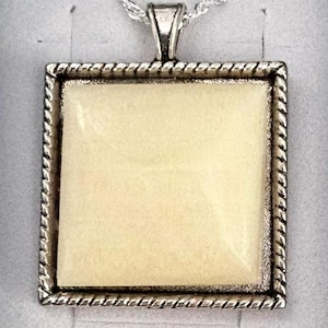 May include: A square pendant necklace featuring a smooth, cream-colored center inlay encased in a silver-toned metal frame with a twisted rope-style border. The pendant hangs from a delicate silver-toned chain attached to a triangular bail.
