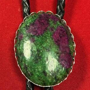 May include: A green and purple gemstone bolo tie with a silver setting and black leather cord.