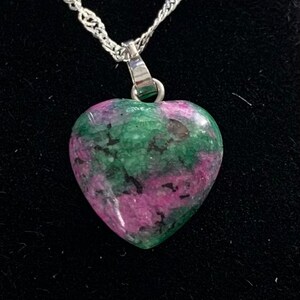 May include: A heart-shaped pendant necklace with a green and pink gemstone. The pendant is made of silver and has a delicate chain.