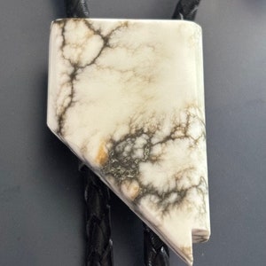May include: A white bolo tie with a black and brown marbled design. The bolo tie is made of a natural material and has a unique, organic look.