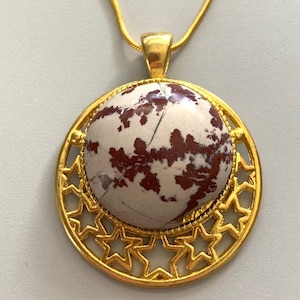 May include: A gold pendant necklace with a round, white and brown stone set in a gold frame with a starburst design.