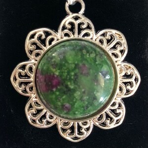 May include: A silver filigree pendant with a green and pink gemstone in the center.