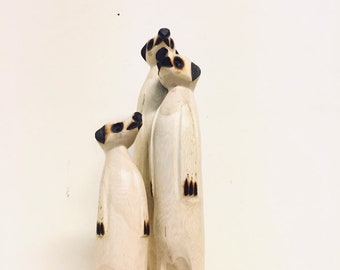 May include: A trio of hand-carved wooden meerkat figurines standing upright in a group. The figures feature a light natural wood grain finish with dark, scorched-effect detailing on the ears, eyes, noses, and paws, creating a high-contrast look.