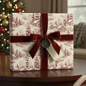 May include: A wrapped gift box featuring a winter village scene in red and cream. It is tied with a burgundy velvet ribbon and bow, with a decorative seal and tag. The gift sits on a dark wooden surface.