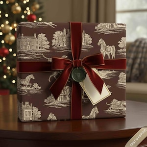 May include: A wrapped gift box with a brown toile design depicting horses, buildings, and trees in white. It's tied with a burgundy velvet ribbon and bow, and a blank tag hangs from a green wax seal.