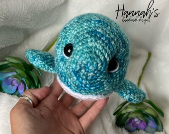 May include: A crocheted blue and white whale with black eyes. The whale is handmade and has a white crocheted belly.