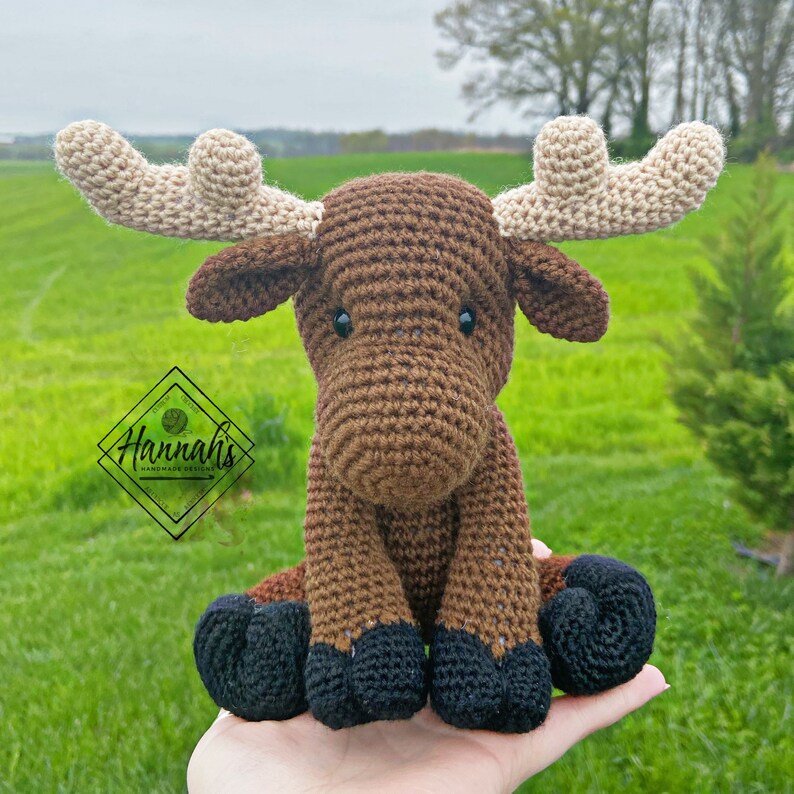 Puede incluir: Un alce de crochet marr&oacute;n con grandes cuernos de color crema. El alce est&aacute; sentado en una mano con sus pezu&ntilde;as negras visibles.