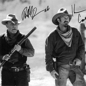 May include: Black and white photograph of two men in cowboy attire, each wearing a hat and holding a rifle. One man holds the rifle, while the other has a holster. Both men have signatures above their heads. The image is from the movie "Open Range (2003)".