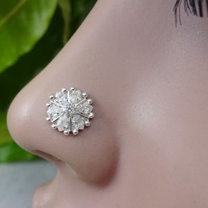 Op de afbeelding: Een zilveren neusring met een rond ontwerp met een centrale steen omgeven door kleinere stenen.