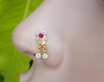 May include: A gold nose ring featuring a flower-shaped design with four clear white stones surrounding a central red stone. Two short gold chains hang from the flower, each ending in a single clear white stone, creating a dangling effect.