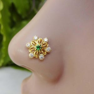 May include: Gold nose ring with a green gem in the center and white stones around it, shaped like a flower.