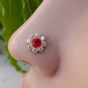 May include: A gold nose ring with a red gemstone surrounded by clear rhinestones in a flower shape.