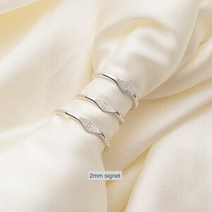 May include: Three silver signet rings with the letters B, M, and R engraved on them. The rings are stacked on top of each other and are sitting on a white fabric background. 2mm signet.