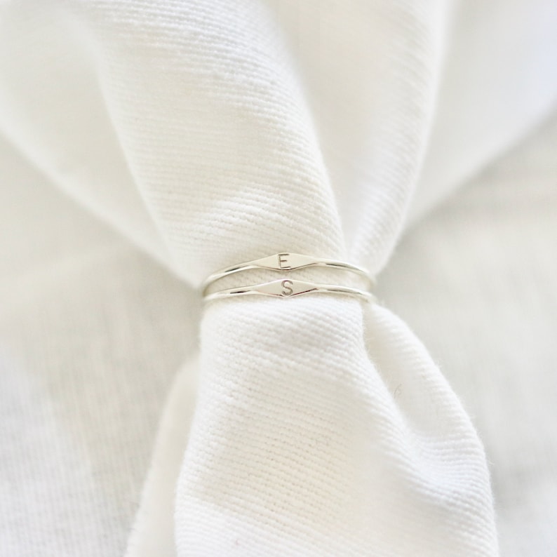 May include: Two silver rings with the letters "E" and "S" engraved on them. The rings are stacked on top of each other and are on a white fabric background.