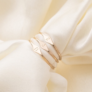 May include: Four gold rings with a diamond-shaped design. Each ring has a different initial engraved on the front: M, J, and R.