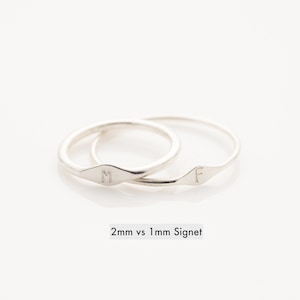May include: Two silver signet rings with the letters "M" and "F" engraved on them. The rings are stacked on top of each other. The caption below the rings reads "2mm vs 1mm Signet".