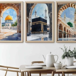 May include: Set of three framed watercolor prints depicting Islamic architecture. The artwork features a golden-domed building, the Kaaba, and a mosque with a green dome. Each print is framed in a light-colored wooden frame, creating a cohesive set.