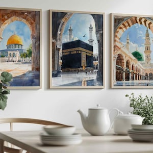 May include: Set of three framed watercolor prints depicting Islamic landmarks. The artwork features the Dome of the Rock, the Kaaba, and the Prophet's Mosque, each framed in a light-colored wooden frame. The paintings showcase architectural details and vibrant colors.