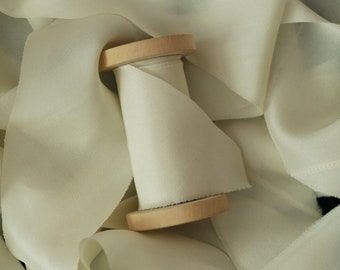 Op de afbeelding: Een spoel met crèmekleurig satijnen lint gewikkeld om een houten spoel. Het lint is zacht en soepel, met een subtiele glans.