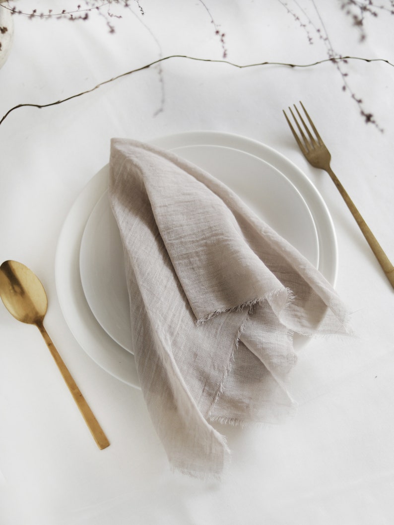 Cotton wedding napkin laying on a table. The fabric is soft and semi - transparent. The color is taupe - subtle blend of gray and brown.