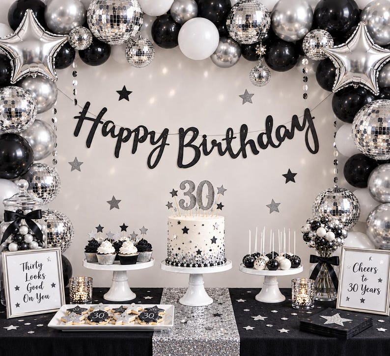 May include: A 30th birthday party display featuring a black and silver balloon arch with disco balls and star balloons. A cake with a 30 topper, cupcakes, and cookies are arranged on white stands. Two signs read Thirty Looks Good On You and Cheers to 30 Years.