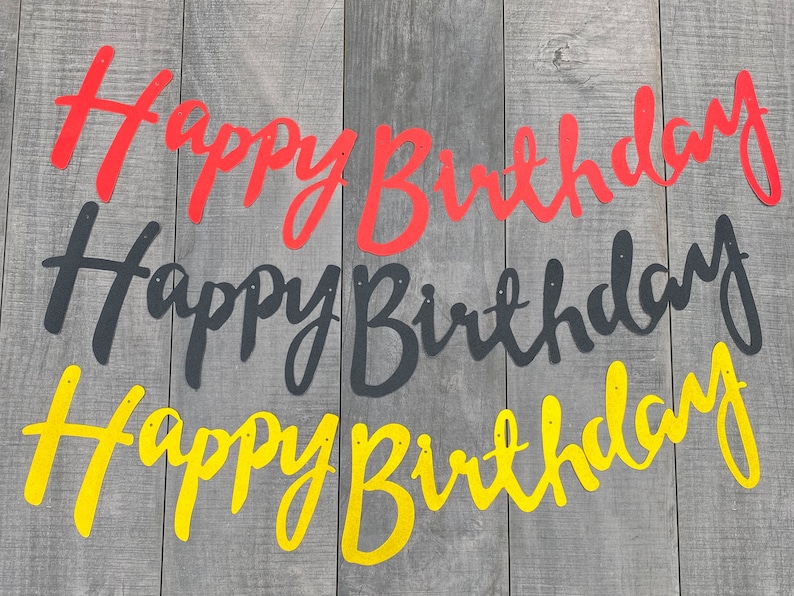 May include: Three separate Happy Birthday banners in cursive script. The top banner is red, the middle banner is black, and the bottom banner is yellow. Each banner features small circular holes at the top for hanging, displayed in a horizontal row.