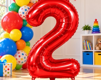 May include: A large, shiny, metallic red foil balloon shaped like the number two. The balloon features a smooth, reflective surface with visible seams along the edges and small tabs at the top and bottom for hanging or securing the decoration.