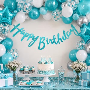 May include: A birthday party display featuring a teal glittery Happy Birthday banner, a balloon arch in teal, white, and silver, a frosted cake with teal accents, cupcakes, gift boxes, and white flowers on a teal sequined tablecloth.