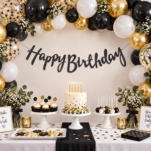 May include: A party display featuring a black Happy Birthday banner, a cake with gold candles, cupcakes, cake pops, and star-shaped cookies. The scene is decorated with black, white, and gold balloons, baby's breath, and two signs reading Make a Wish and Good Vibes Only.