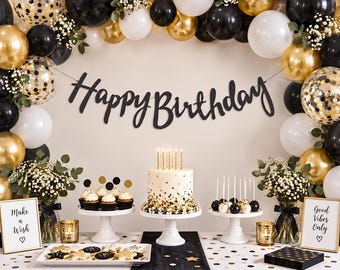 May include: A party display featuring a black Happy Birthday banner, a cake with gold candles, cupcakes, cake pops, and star-shaped cookies. The scene is decorated with black, white, and gold balloons, baby's breath, and two signs reading Make a Wish and Good Vibes Only.