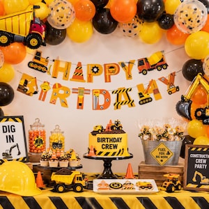 May include: A construction-themed party display featuring a Happy Birthday banner, a yellow cake labeled Birthday Crew, a yellow hard hat, toy dump trucks, cookies, and a metal bucket labeled Fuel for Big Work, all decorated with black and yellow balloons.
