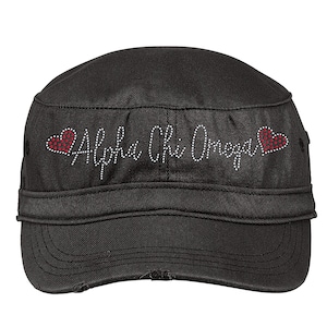 May include: Black canvas military style cap with a white rhinestone design that reads "Alpha Chi Omega" with a red rhinestone heart on each side.
