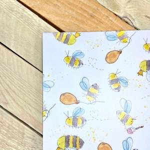 May include: White wrapping paper with a repeating pattern of yellow and black bees with brown balloons and gold glitter.