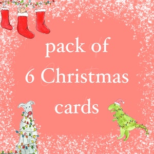 May include: A pack of 6 Christmas cards featuring a dinosaur and a dog wearing Christmas lights. The cards have a pink background with white snowflakes.
