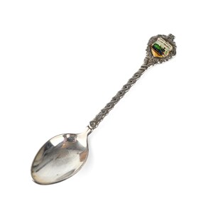May include: Silver souvenir spoon with an ornate handle and a colourful enamel design featuring a scene from the city of Galway, Ireland.